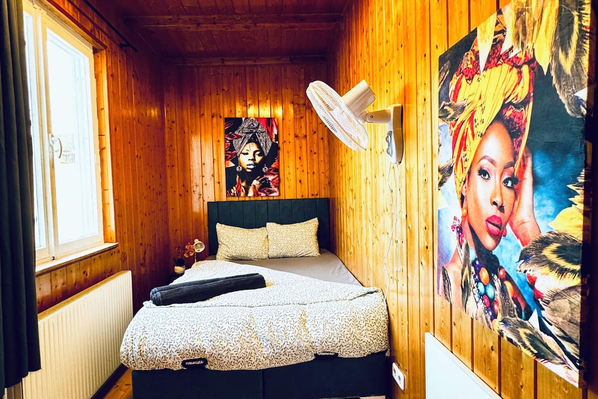 Een knus houten vertrek met een bed, een plafondventilator, een radiator en een groot schilderij aan de muur.