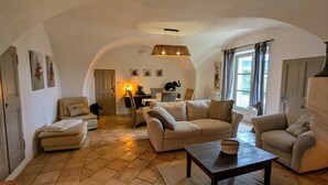Een ruime woonkamer met een hoge plafond, een open haard en een eethoek met rieten meubels.
