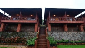 A symmetrical building with two levels, a central staircase, and a stone wall with greenery. - Waves and Vibes Resort (Pune)
