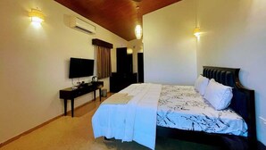 A bedroom with a bed, a TV, a desk, and a ceiling fan. - Waves and Vibes Resort (Pune)