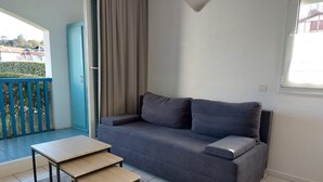 A modern living room with a grey sofa, a wooden coffee table, and a view of a balcony with a blue railing.