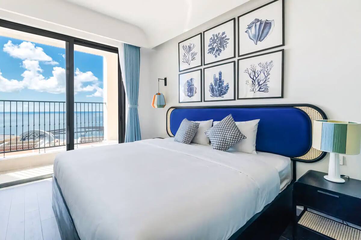 Une chambre d’hôtel avec un grand lit, une vue sur la mer et des œuvres d’art encadrées au mur.