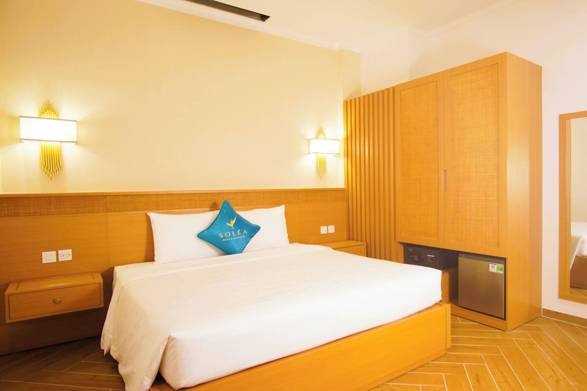 Une chambre d’hôtel avec un grand lit, une armoire en bois, des tables de chevet et des lampes fixées au mur.