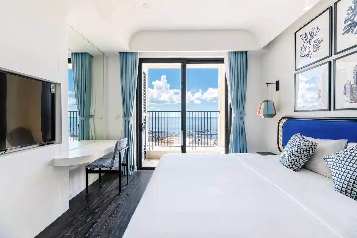 Une chambre d’hôtel équipée d’un lit, d’un bureau, d’une chaise, d’une télévision et d’un balcon avec vue sur la mer.