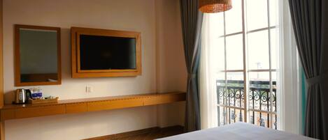 Habitación de hotel con una cama grande, un estante de madera con artículos de aseo, televisión y ventana con vistas al balcón.