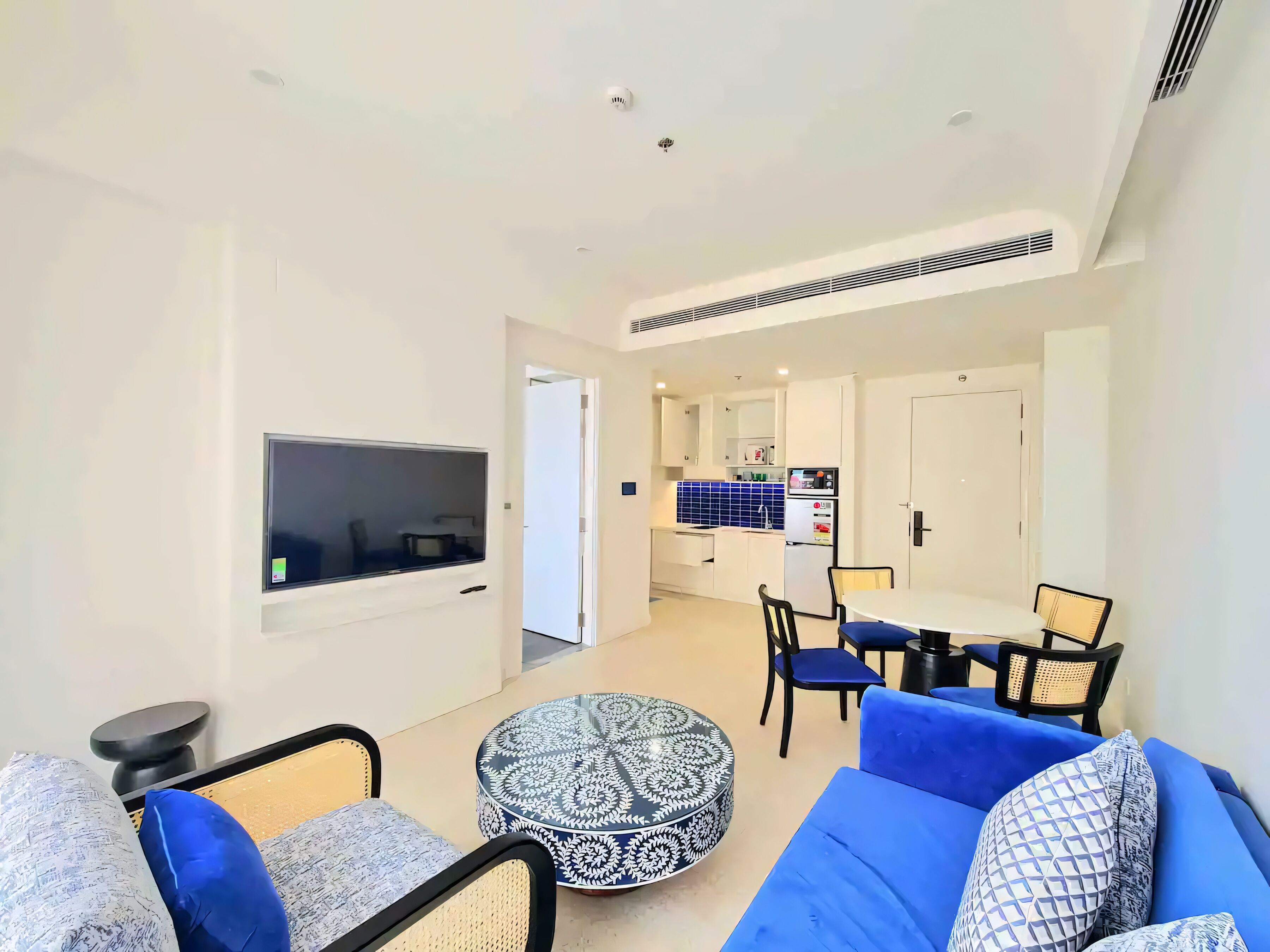 A modern living room with a TV, sofa, ottoman, and dining area with chairs.