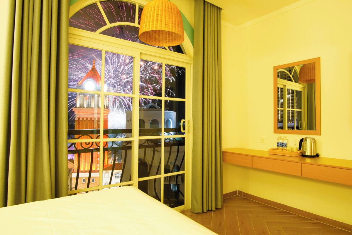 Une chambre d’hôtel avec une grande fenêtre, un lit, une table de chevet avec une bouilloire et un miroir au mur.