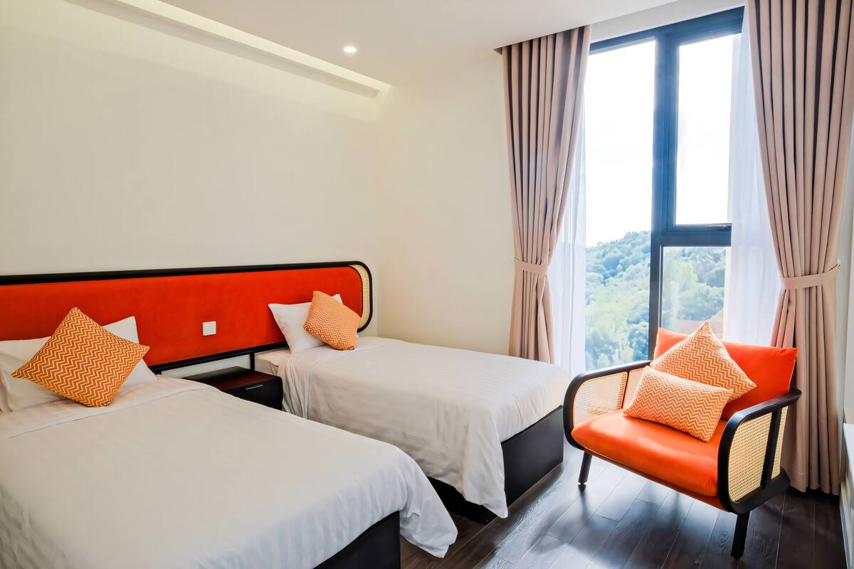 Une chambre d’hôtel avec deux lits, une chaise et une grande fenêtre avec des rideaux.