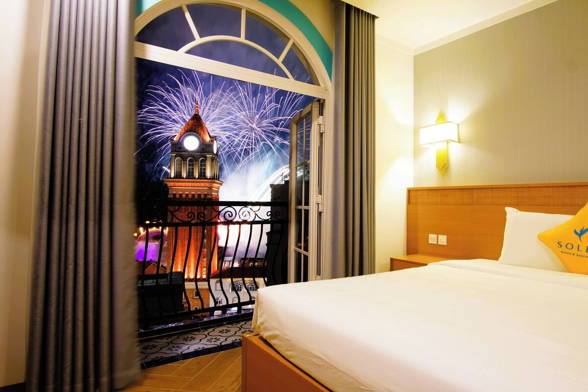 Une chambre d’hôtel avec un lit, une table de chevet, une lampe fixée au mur et une fenêtre avec des rideaux.