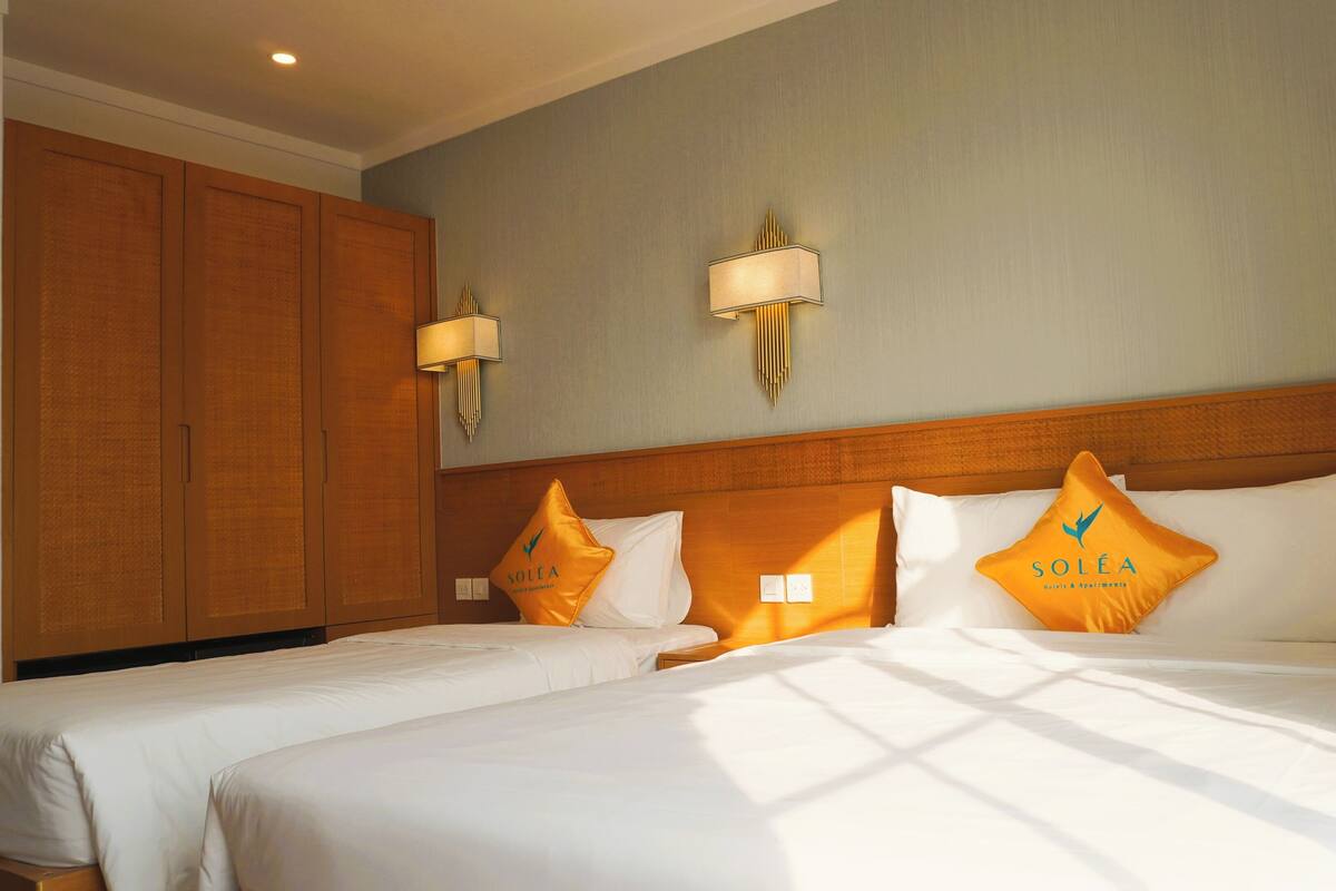 Une chambre d’hôtel avec deux lits, une tête de lit en bois et deux lampes fixées au mur.