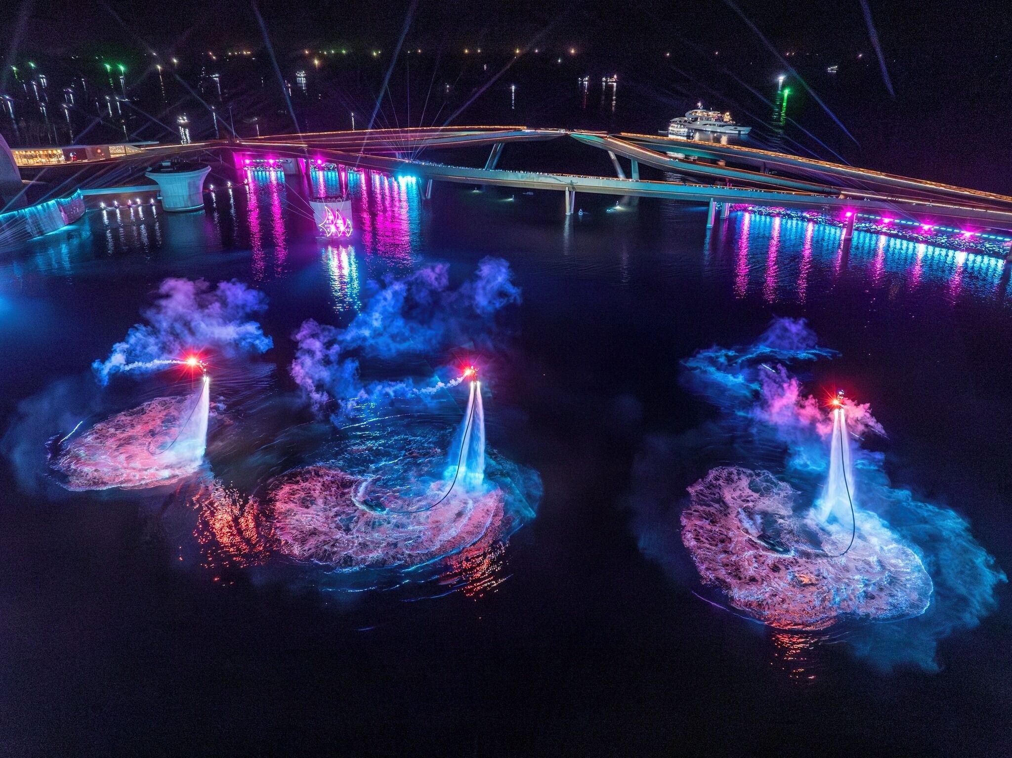 A nighttime view of a bridge with colorful lights reflecting on the water.