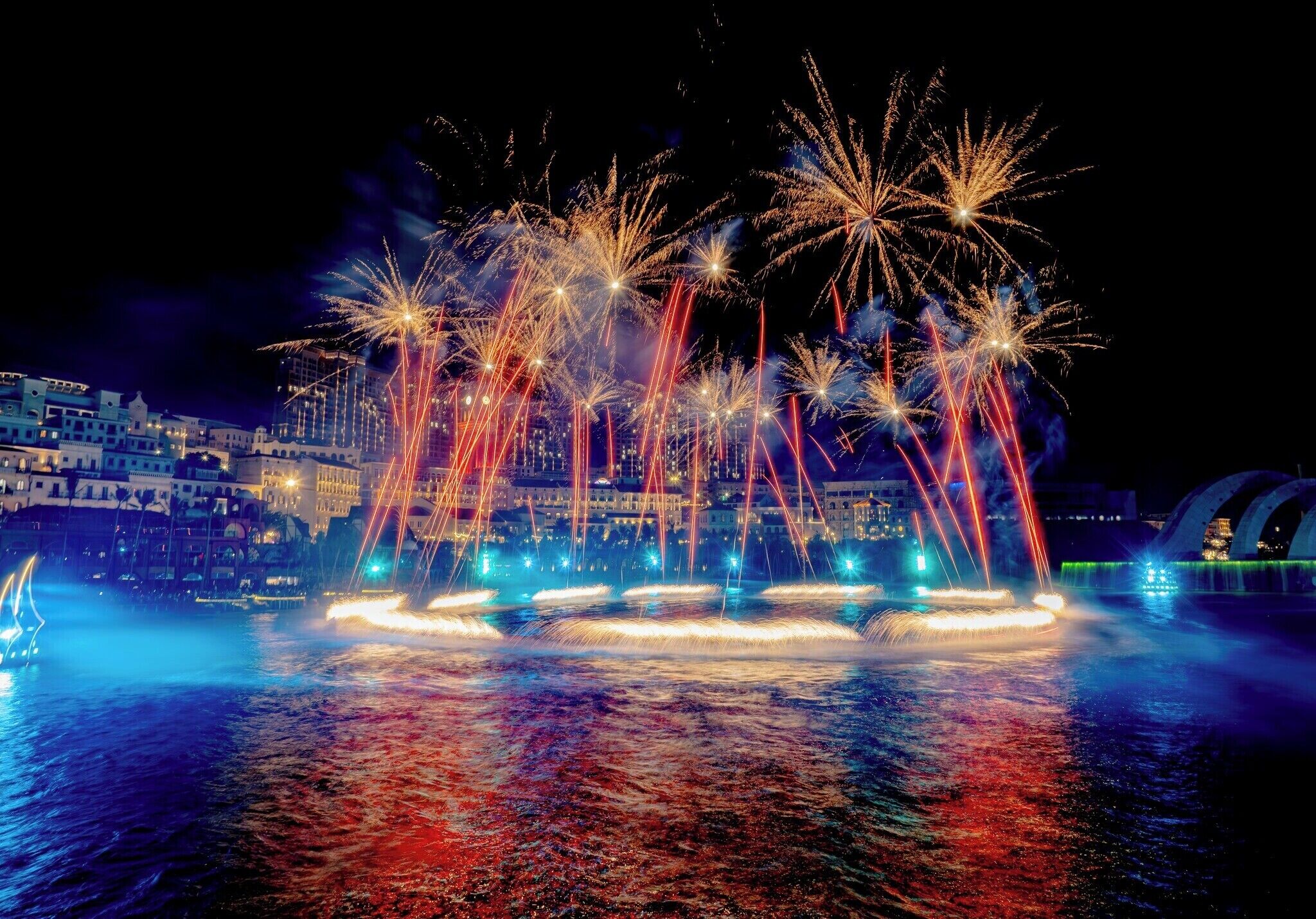 A nighttime view of a waterfront with fireworks display and illuminated buildings.