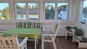 A room with a dining table, chairs, and a bench with plaid cushions. There are windows with views of houses and trees. - The vacation apartment close to nature invites you to experience a vacation in the heart of nature (Ruderting)