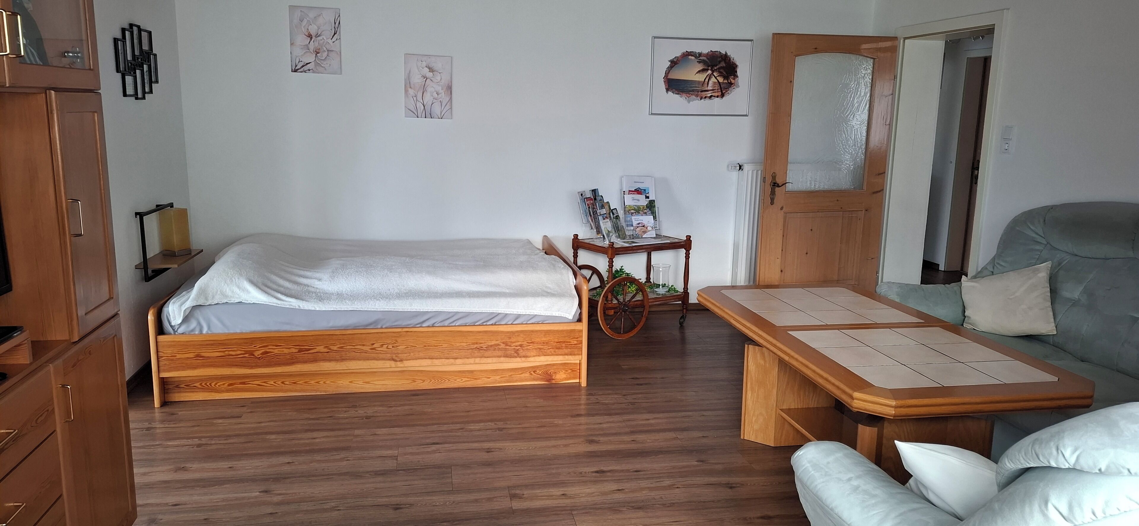 A room with a wooden bed, a sofa, a small table with magazines, and a door leading to another room.
