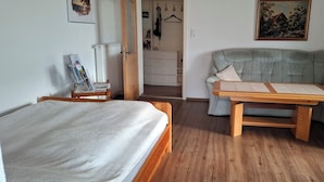 A room with a bed, a wooden table, a grey sofa, and a white dresser. - The vacation apartment close to nature invites you to experience a vacation in the heart of nature (Ruderting)