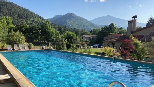 Una piscina con agua azul cristalina, rodeada de abundante vegetación y un telón de fondo montañoso.