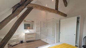 A bedroom with a sloped ceiling, a bed with a yellow blanket, a white dresser, a mirror, and a white wardrobe.