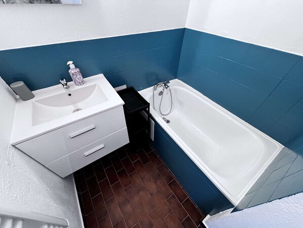 Une salle de bain avec un lavabo blanc, un miroir, un flacon de gel hydroalcoolique et une baignoire.