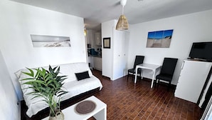 A compact living space with a sofa, a small table, a TV, and a kitchenette in the background. - Quiet Studio Cabin, Canal View, Near Beach and Shops (Cap d'Agde)