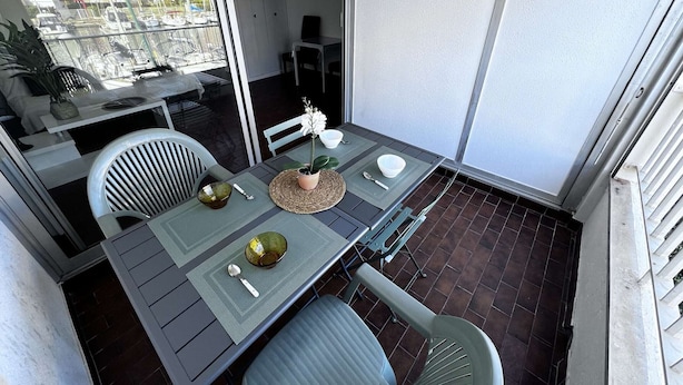 A balcony with a table set for two, chairs, and a potted plant. - Quiet Studio Cabin, Canal View, Near Beach and Shops (Cap d'Agde)