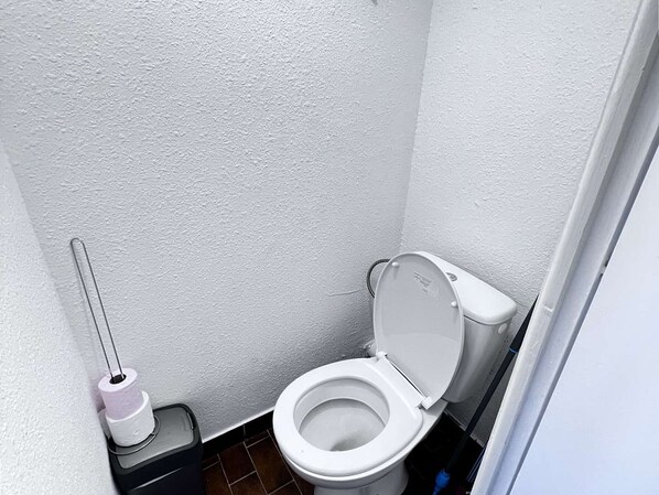 A small, white-walled bathroom with a white toilet, a toilet paper holder, and a trash bin. - Quiet Studio Cabin, Canal View, Near Beach and Shops (Cap d'Agde)