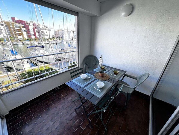 Un balcon avec une table dressée pour deux personnes, une chaise et une vue sur une marina remplie de bateaux.