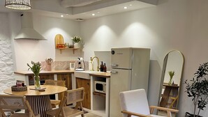 Une cuisine moderne équipée d’un four à micro-ondes, d’un évier et d’un réfrigérateur en acier inoxydable. On y trouve un coin repas avec une table ronde et des chaises, ainsi qu’un canapé agrémenté d’un plaid rouge.