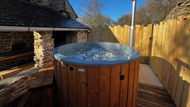 Un bain à remous en bois installé dans un jardin, avec des murs en pierre et une terrasse en bois.