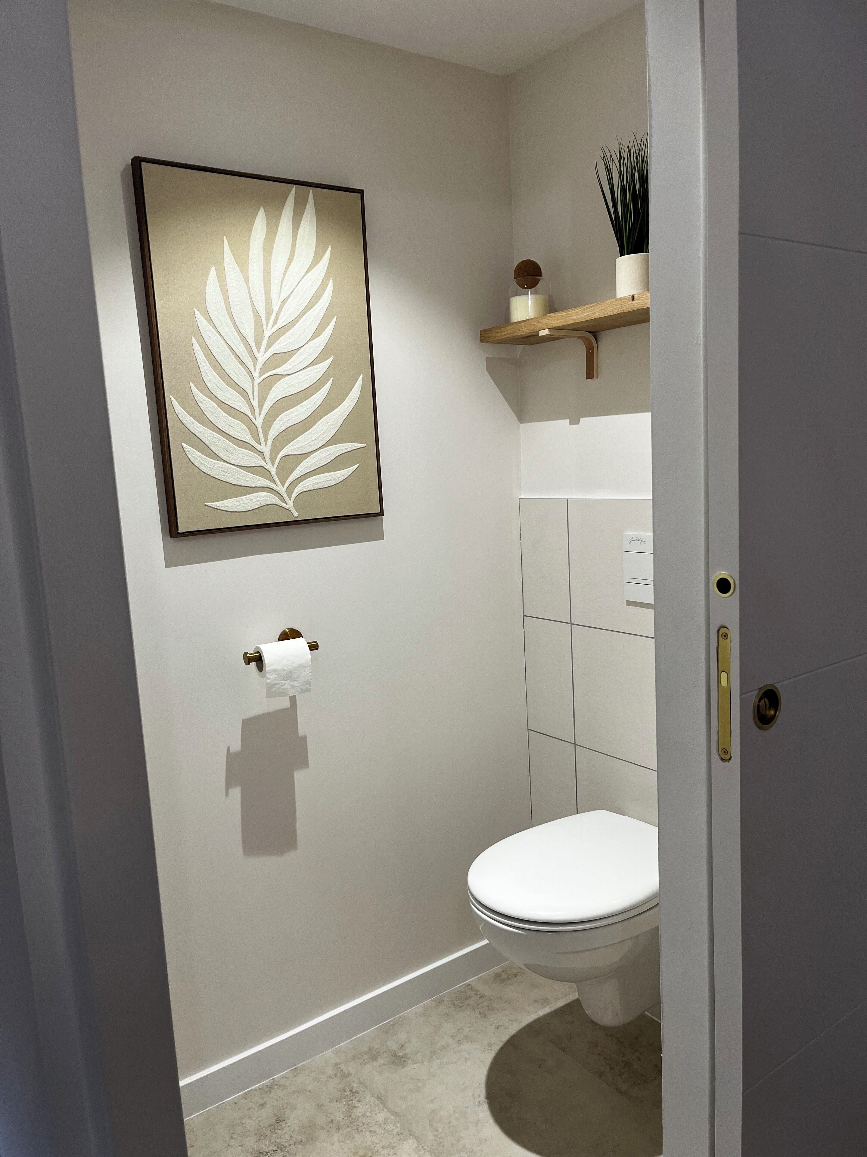 Une salle de bain équipée de toilettes, d’un porte-serviettes et d’une œuvre d’art représentant une feuille, encadrée et accrochée au mur.
