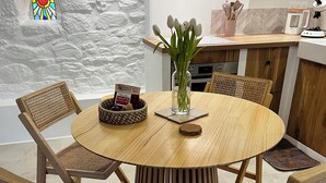 Une table de salle à manger ronde en bois, entourée de six chaises en osier, un vase rempli de fleurs et un petit panier contenant un livre.
