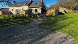 Une maison en pierre avec une allée en gravier, une clôture en bois et une pelouse bien entretenue.