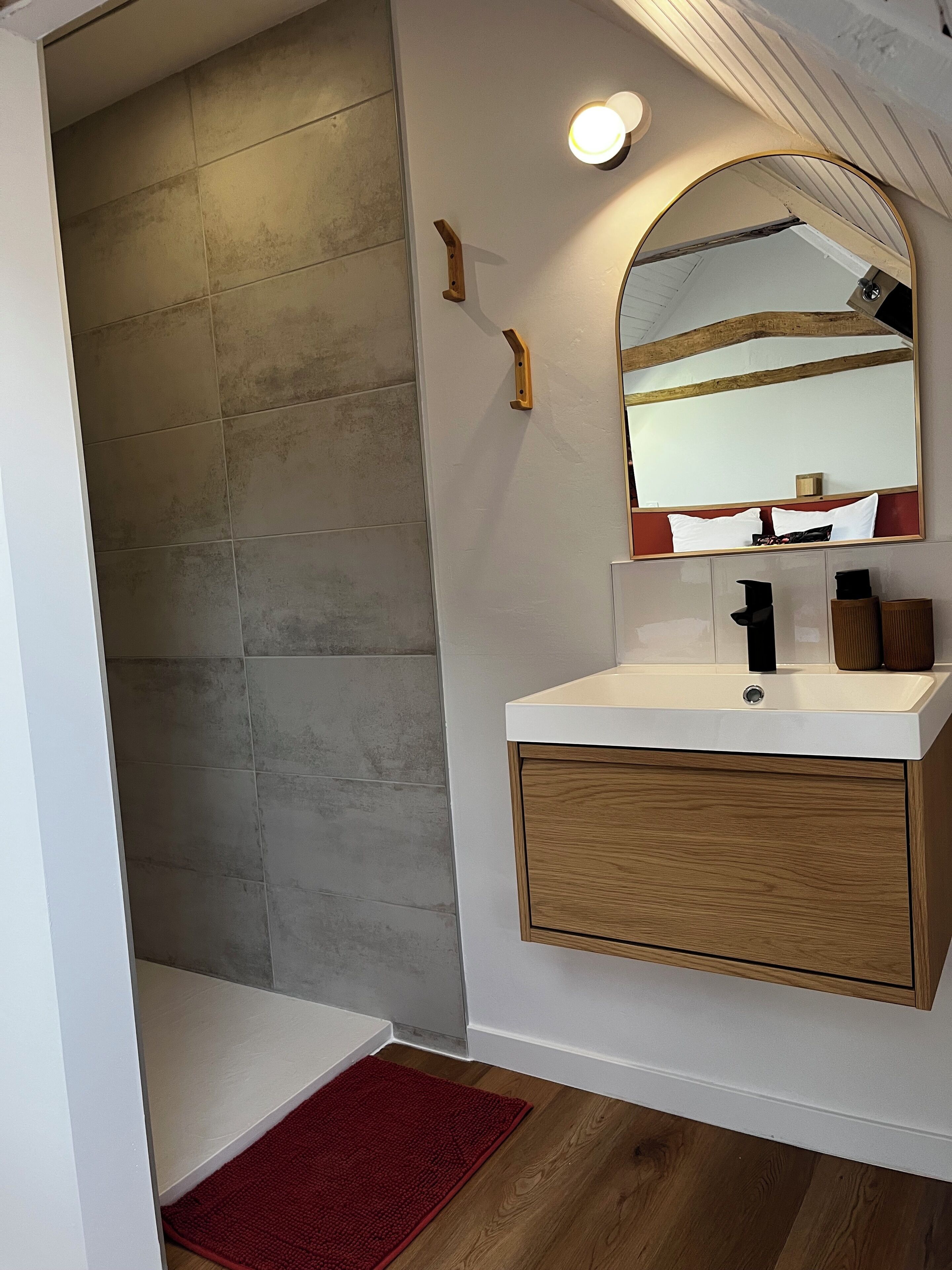 A bathroom with a white vanity, a mirror, and a shower area with grey tiles.