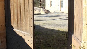 Una puerta de madera que da a un edificio con fachada de piedra, una ventana pequeña y un patio de grava.