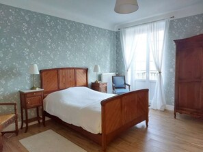 Ein Schlafzimmer mit einem hölzernen Bett, zwei Nachttischen mit Lampen, einem Sessel, einem Kleiderschrank und einem Fenster mit Vorhängen.