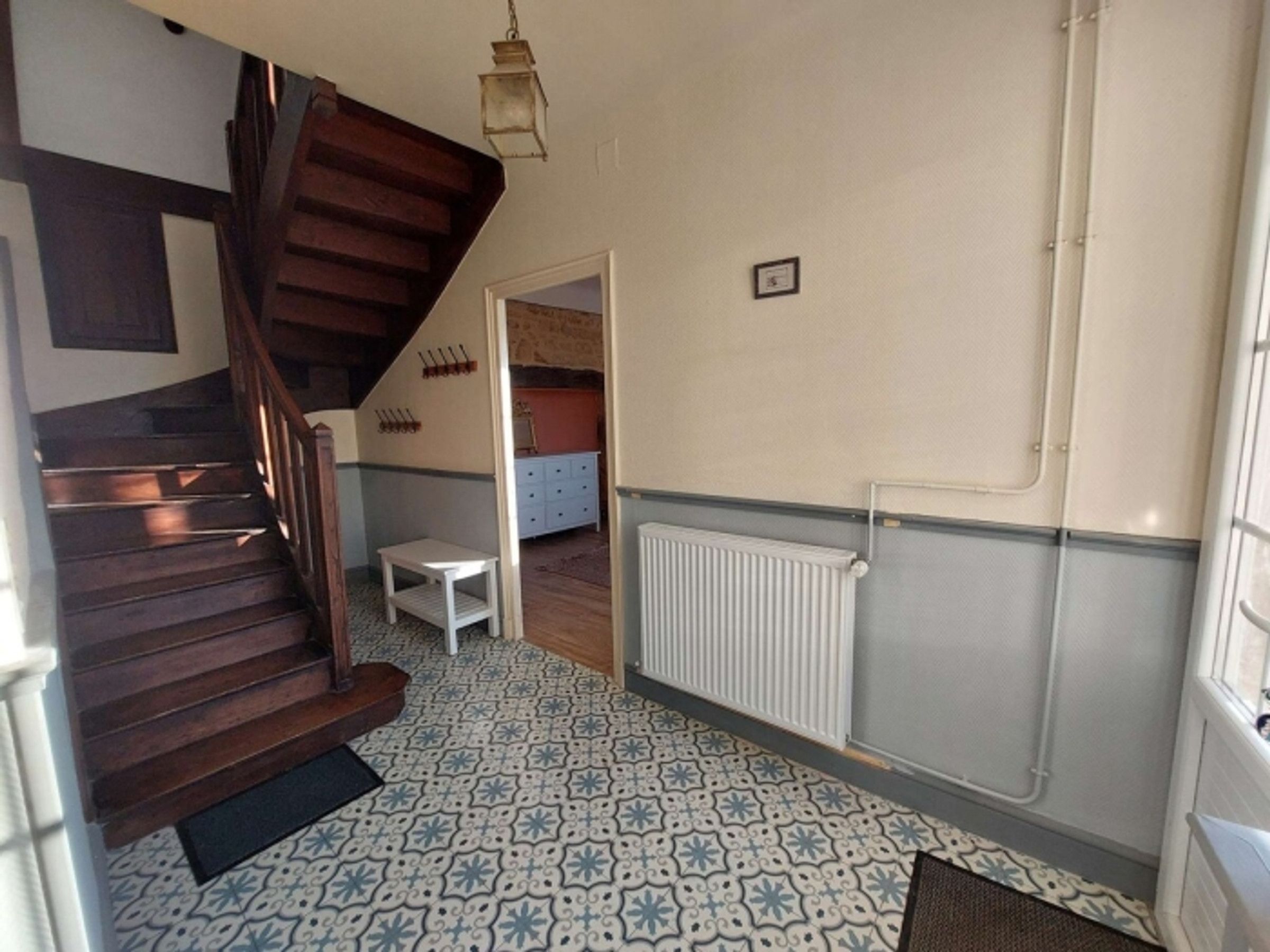 Una habitación con una escalera de madera, un radiador, un suelo estampado y una pequeña mesa.
