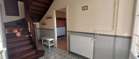 Una habitación con una escalera de madera, un radiador, un suelo estampado y una pequeña mesa.
