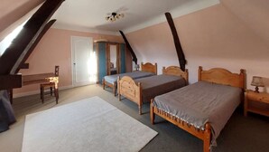 Un dormitorio con dos camas de madera, una alfombra blanca, una silla de madera y una pequeña mesa con una lámpara.
