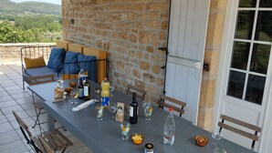 Un espacio exterior para comer con paredes de piedra, una mesa dispuesta con comida y bebidas, y un sofá con cojines.