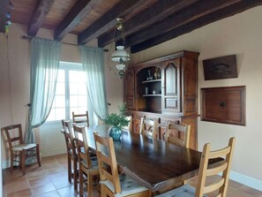 Ein Esszimmer mit Holztisch und -stühlen, einem Schrank mit Gläsern und einem Fenster mit Vorhängen.