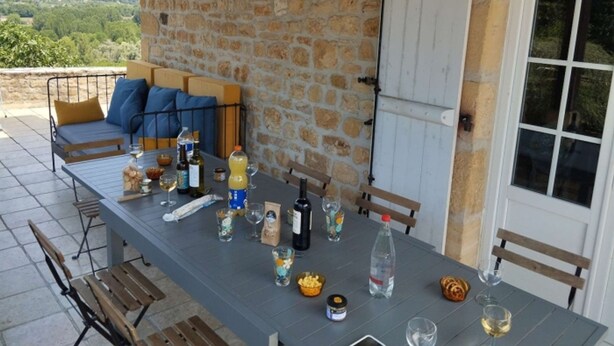 Un área de comedor al aire libre con una pared de piedra, una mesa dispuesta con diversos objetos y vistas al campo.