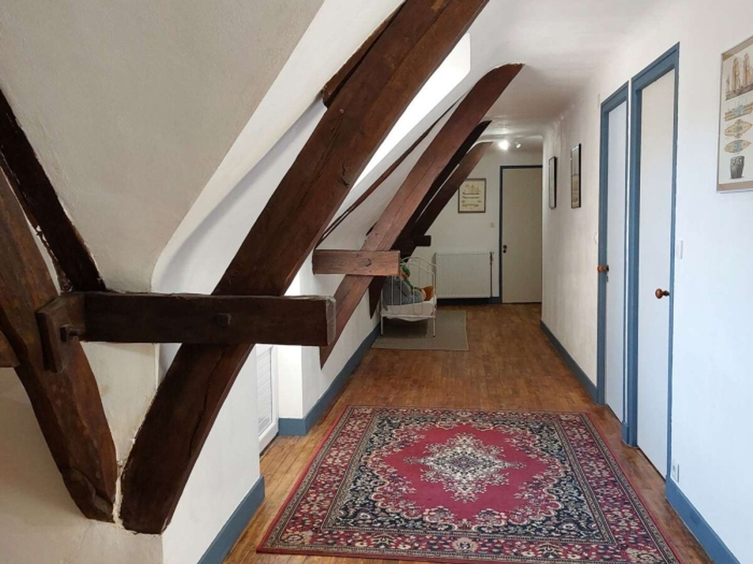 Un pasillo con vigas de madera, un tapete estampado y una puerta con detalles azules.