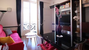 A modern living room with a red sofa, a glass dining table, and a bookshelf. - Central La Bourboule T2 Apartment, 4 pers, Wifi (La Bourboule)
