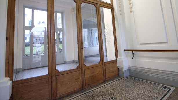 A room with a large wooden cabinet with glass doors, a patterned rug, and a white wall with decorative molding. - Central La Bourboule T2 Apartment, 4 pers, Wifi (La Bourboule)