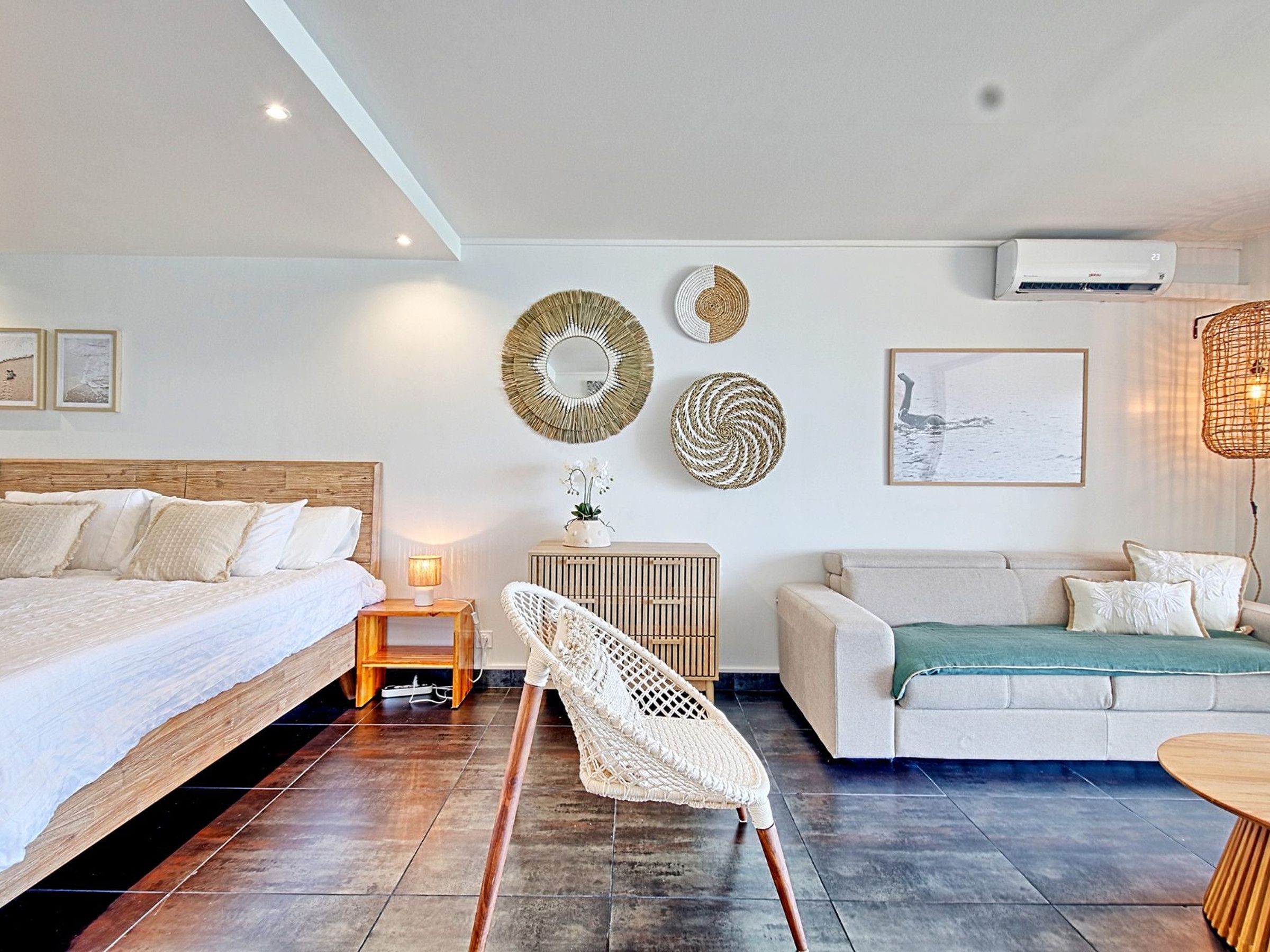 A modern hotel room with a bed, a chair, a sofa, a table, and decorative wall art.