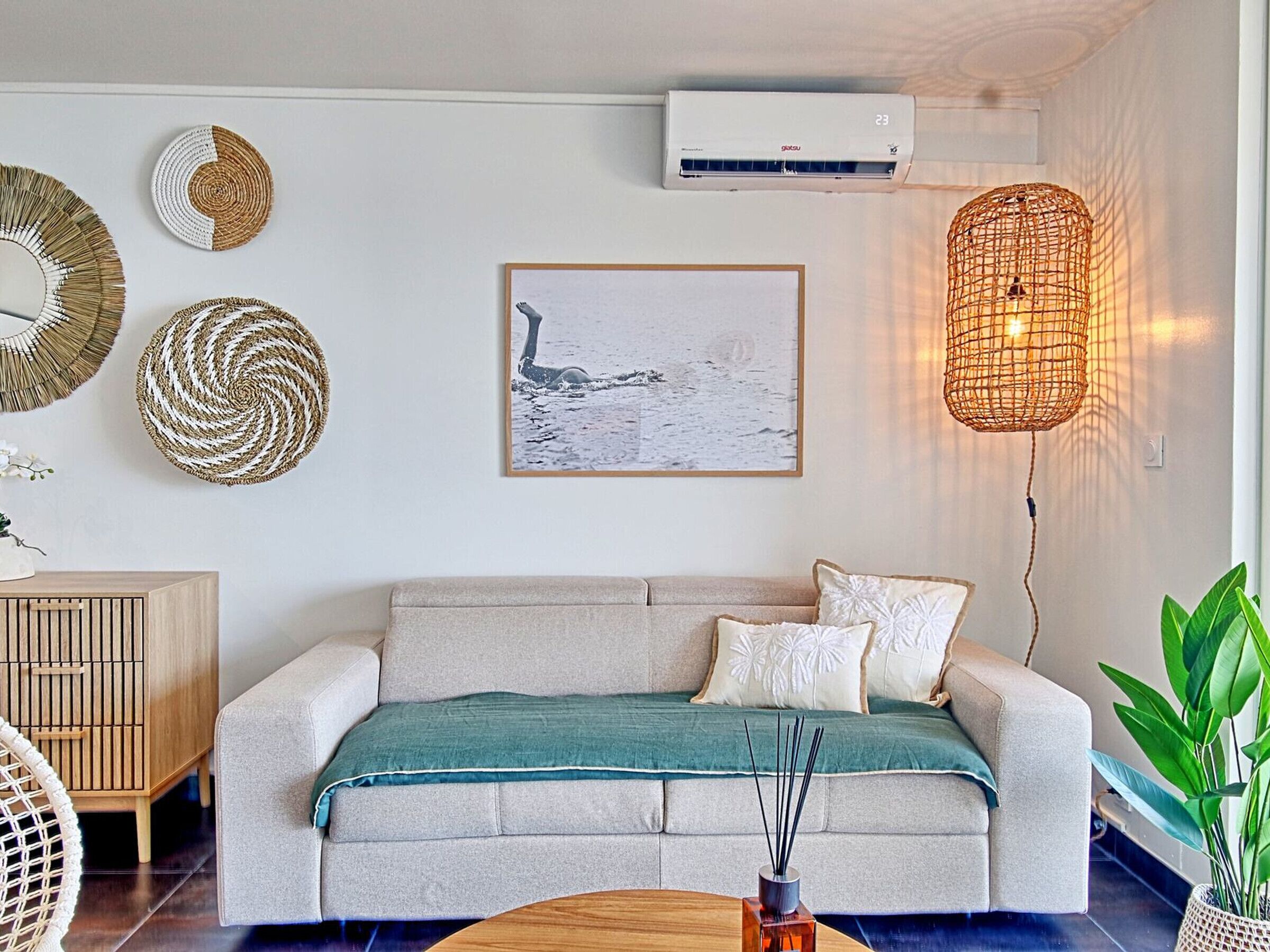 Un salon moderne avec un canapé beige, une table d’appoint en bois et une lampe en fibres tressées.
