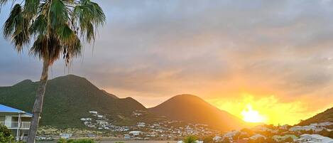 A coastal town with a sunset, palm trees, and a mountain in the background.