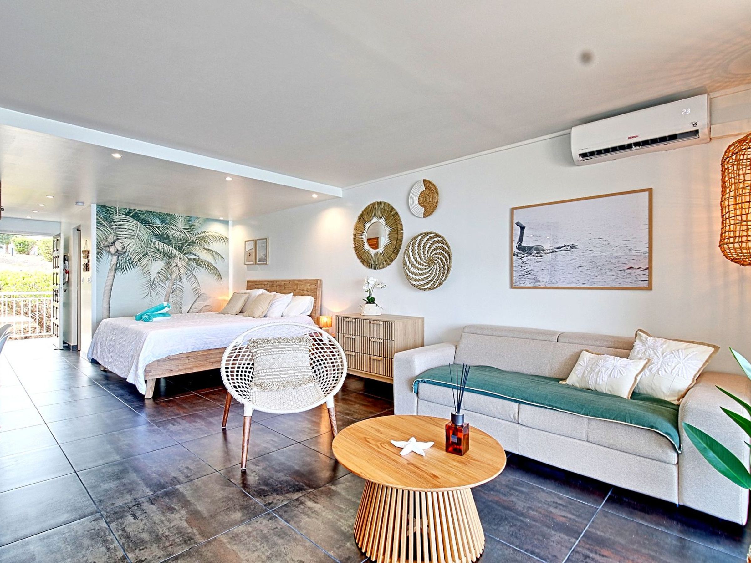 A modern bedroom with a bed, a sofa, a round wooden table, and a large window.