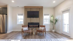 A modern living room with a fireplace, two armchairs, a coffee table, and a large TV.