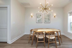 Un espace repas comprenant une table et des chaises en bois, un lustre moderne et des luminaires fixés au mur.