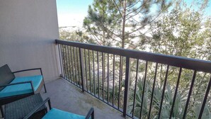 A balcony with a metal railing, two wicker chairs with blue cushions, and a view of trees and a building in the background. - Beachside Bliss-Minutes from Beach, Pool, Hot Tub, Near Golf (Miramar Beach)